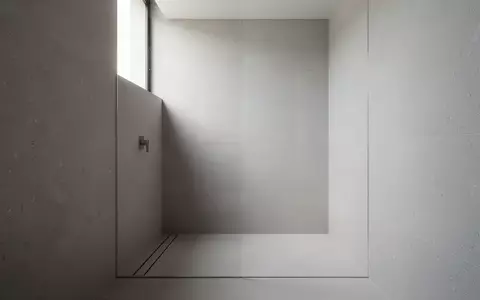 Minimalistisches Badezimmer mit nahtlosen grauen Steinoberflächen, ebenerdiger Dusche und architektonischer Klarheit. - Foto: über boerse-global.de