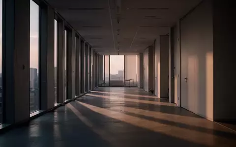 Ein leerer, minimalistischer Flur in einem modernen Bürogebäude bei Dämmerung mit langen Schatten und weichem Lichteinfall. - Foto: über boerse-global.de