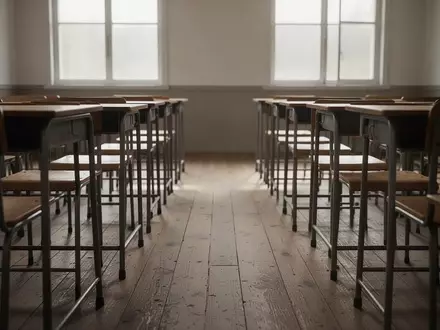 Ein leerer Klassenraum mit Holzschulbänken und Stühlen in natürlichem Tageslicht. - Foto: über boerse-global.de