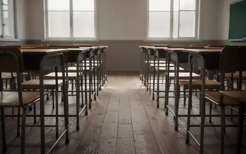 Ein leerer Klassenraum mit Holzschulbänken und Stühlen in natürlichem Tageslicht. - Foto: über boerse-global.de