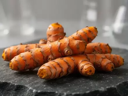 Frische Kurkumawurzeln liegen auf einer dunklen Steinoberfläche vor einem unscharfen Laborhintergrund. - Foto: über boerse-global.de