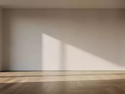 Ein minimalistisches, modernes Wohnzimmer mit leerer Wand und sanftem Lichteinfall. - Foto: über boerse-global.de