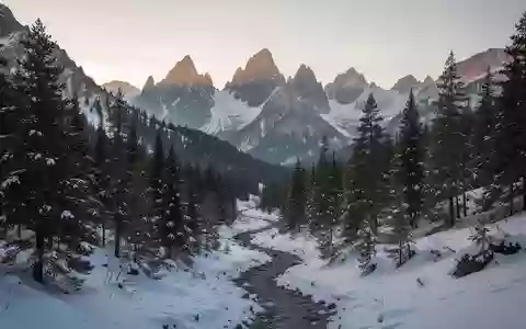 Eine verschneite Berglandschaft mit einem kurvigen Pfad durch einen Nadelwald bei Sonnenaufgang. - Foto: über boerse-global.de