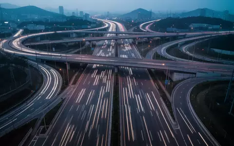 Ein weitläufiges Autobahnkreuz bei Dämmerung mit klaren Fahrbahnmarkierungen und geschwungenen Kurven in einer urbanen Umgebung. - Foto: über boerse-global.de
