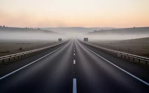 Eine leere Autobahn bei nebligem Morgengrauen erstreckt sich durch eine weite Landschaft. - Foto: über boerse-global.de