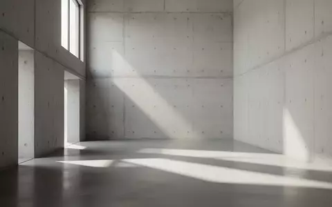 Ein minimalistischer, leerer Raum mit Sichtbetonwänden und geometrischen Licht- und Schattenwürfen durch ein hohes Fenster. - Foto: über boerse-global.de