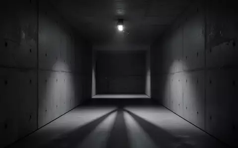 Ein düsterer, minimalistischer Flur in einem modernen Betongebäude mit einem flackernden Licht, das lange Schatten wirft. - Foto: über boerse-global.de