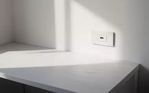 Ein minimalistischer, leerer Schreibtisch mit einer einzelnen USB-C-Buchse in der Wand bei natürlichem Licht. - Foto: über boerse-global.de