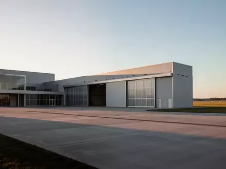 Ein moderner Flugzeughangar auf einem Flugplatz bei Sonnenuntergang mit einer leeren Rollbahn im Vordergrund. - Foto: über boerse-global.de