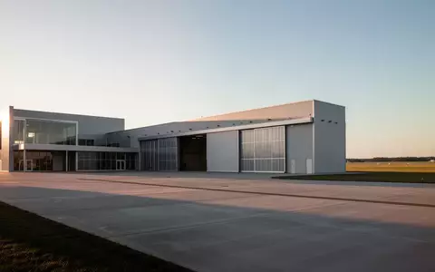 Ein moderner Flugzeughangar auf einem Flugplatz bei Sonnenuntergang mit einer leeren Rollbahn im Vordergrund. - Foto: über boerse-global.de