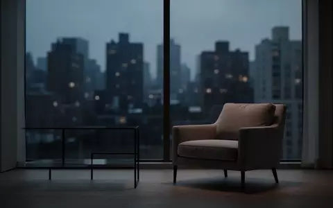 Ein leerer Sessel in einem minimalistisch eingerichteten Raum bei Dämmerung mit Blick auf eine nächtliche Stadtlandschaft. - Foto: über boerse-global.de