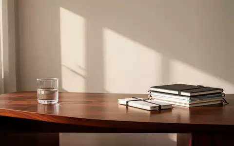 Ein minimalistischer Arbeitsplatz mit einem Holztisch, Notizbüchern und natürlichem Licht. - Foto: über boerse-global.de