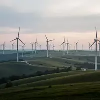 Weitläufige Windkraftanlage auf einer grünen Hügellandschaft in der Abenddämmerung. - Foto: über boerse-global.de