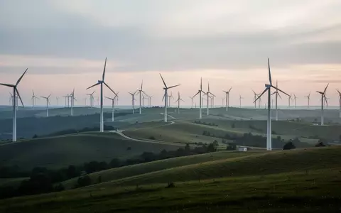 Weitläufige Windkraftanlage auf einer grünen Hügellandschaft in der Abenddämmerung. - Foto: über boerse-global.de