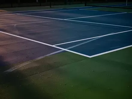 Ein professioneller Tennisplatz mit blauen und grünen Bodenbelägen und weißen Linien bei Dämmerung. - Foto: über boerse-global.de