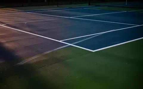 Ein professioneller Tennisplatz mit blauen und grünen Bodenbelägen und weißen Linien bei Dämmerung. - Foto: über boerse-global.de