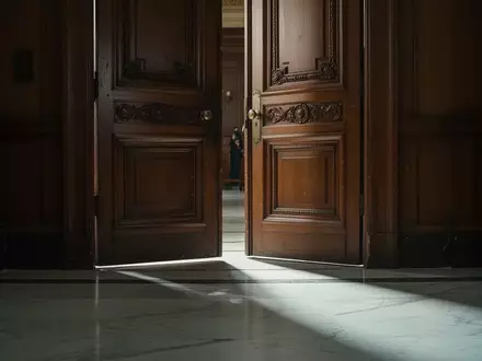 Eine schwere Holztür in einem Gerichtssaal mit einfallendem Licht auf einem Marmorboden. - Foto: über boerse-global.de