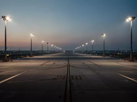 Weitläufiges, leeres Vorfeld eines Flughafens bei Dämmerung mit Bodenmarkierungen und Flutlichtbeleuchtung. - Foto: über boerse-global.de