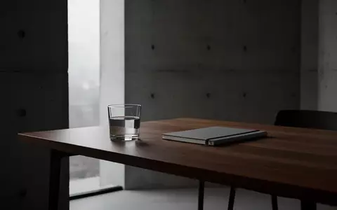 Ein minimalistischer, ruhiger Arbeitsplatz mit einem Holztisch vor einer Betonwand bei natürlichem Licht. - Foto: über boerse-global.de