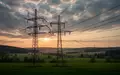 Ein Hochspannungsmast steht in einer weiten, hügeligen Landschaft bei Sonnenuntergang. - Foto: über boerse-global.de