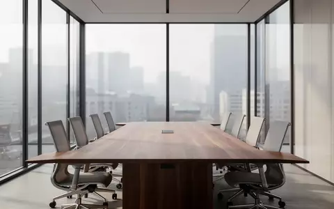 Ein minimalistischer, moderner Konferenzraum mit einem langen Holztisch und leeren Stühlen vor einer Fensterfront. - Foto: über boerse-global.de