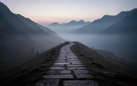 Ein einsamer, steiniger Pfad, der sich durch eine neblige Berglandschaft in der Morgendämmerung schlängelt. - Foto: über boerse-global.de