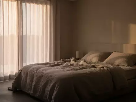 Ein minimalistisches Schlafzimmer in der Morgendämmerung mit weichem Tageslicht, das auf ein ungemachtes Bett fällt. - Foto: über boerse-global.de