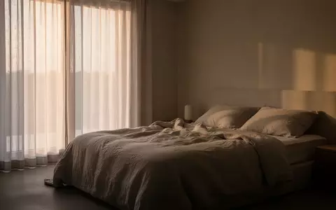 Ein minimalistisches Schlafzimmer in der Morgendämmerung mit weichem Tageslicht, das auf ein ungemachtes Bett fällt. - Foto: über boerse-global.de