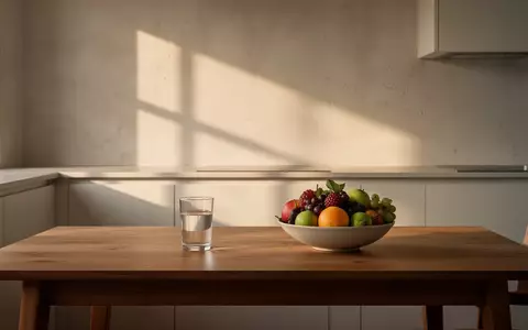 Ein minimalistischer, sonnendurchfluteter Küchentisch mit einem Glas Wasser und einer Schale frischem Obst am Morgen. - Foto: über boerse-global.de