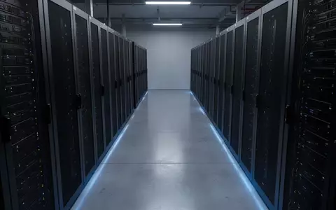 Reihen von dunklen Server-Racks in einem modernen Rechenzentrum mit bläulicher Beleuchtung auf einem polierten Boden. - Foto: über boerse-global.de