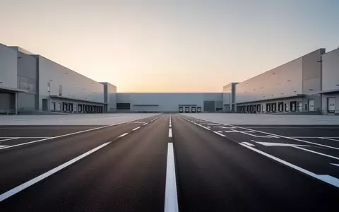 Weitläufiges, modernes Logistikgelände bei Dämmerung mit präzisen Fahrbahnmarkierungen und minimalistischen Industriehallen. - Foto: über boerse-global.de
