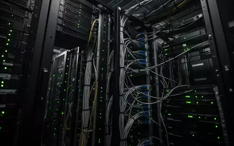 Reihen von Server-Racks in einem dunklen Rechenzentrum mit leuchtenden Statusanzeigen und geordneten Netzwerkkabeln. - Foto: über boerse-global.de