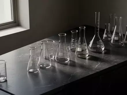 Minimalistische Laborumgebung mit Glasgefäßen auf einer dunklen, polierten Oberfläche in natürlichem Licht. - Foto: über boerse-global.de