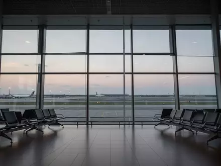 Leerer Abflugbereich eines modernen Flughafens mit Blick auf das Rollfeld bei Dämmerung. - Foto: über boerse-global.de