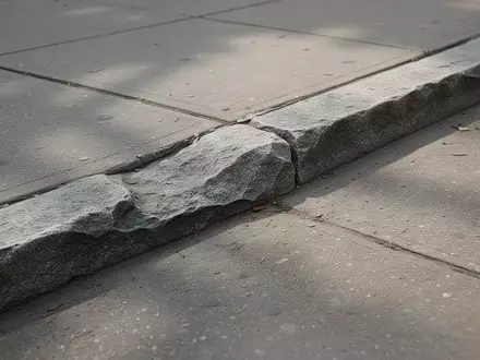 Ein leicht unebener Übergang zwischen zwei Gehwegplatten aus Beton in einer städtischen Umgebung bei Tageslicht. - Foto: über boerse-global.de