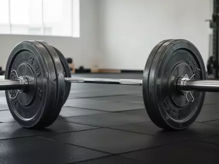 Eine schwere Langhantel mit Hantelscheiben auf einem dunklen Boden in einem minimalistischen Fitnessraum. - Foto: über boerse-global.de