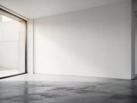 Ein minimalistischer, lichtdurchfluteter Raum mit poliertem Betonboden und einer leeren weißen Wand. - Foto: über boerse-global.de