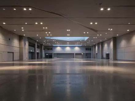 Weitwinkelaufnahme einer leeren Messehalle mit minimalistischer Architektur und polierten Betonböden in der Abenddämmerung. - Foto: über boerse-global.de