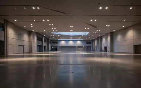 Weitwinkelaufnahme einer leeren Messehalle mit minimalistischer Architektur und polierten Betonböden in der Abenddämmerung. - Foto: über boerse-global.de