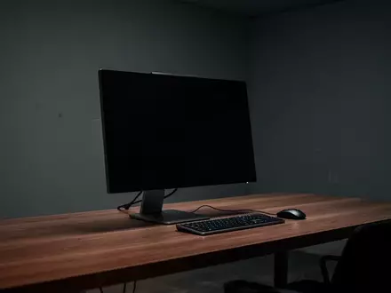 Ein minimalistischer Arbeitsplatz mit einem ausgeschalteten Monitor in einem abgedunkelten Raum. - Foto: über boerse-global.de