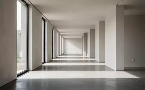 Ein minimalistischer, leerer Flur mit modernen Architekturmerkmalen und natürlichem Lichteinfall durch große Fenster. - Foto: über boerse-global.de