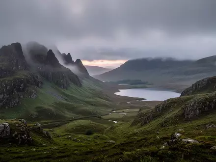 Eine weitläufige, neblige Landschaft in den schottischen Highlands mit sanften grünen Hügeln und einem ruhigen See. - Foto: über boerse-global.de