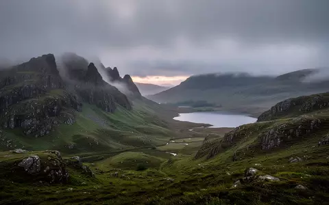 Eine weitläufige, neblige Landschaft in den schottischen Highlands mit sanften grünen Hügeln und einem ruhigen See. - Foto: über boerse-global.de