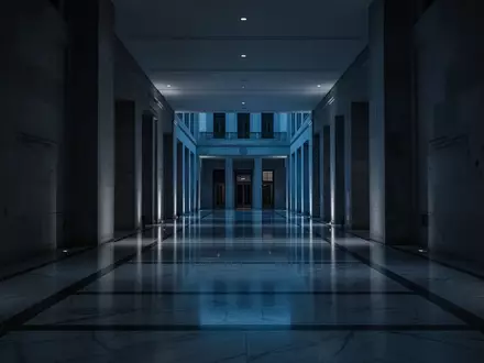 Ein dunkler, minimalistischer Flur eines Regierungsgebäudes in der Dämmerung mit tiefen Schatten und bläulichem Licht. - Foto: über boerse-global.de