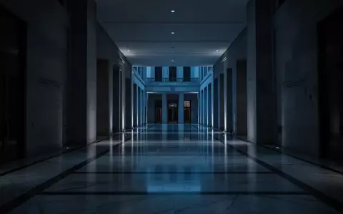 Ein dunkler, minimalistischer Flur eines Regierungsgebäudes in der Dämmerung mit tiefen Schatten und bläulichem Licht. - Foto: über boerse-global.de
