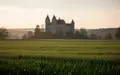Eine weitläufige grüne Wiese mit einem Schloss im fernen Hintergrund bei Sonnenuntergang. - Foto: über boerse-global.de