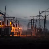 Ein dunkles, industrielles Stromnetz-Gelände bei Dämmerung mit glühenden Transformatoren und Hochspannungsleitungen in einer nebligen Landschaft. - Foto: über boerse-global.de