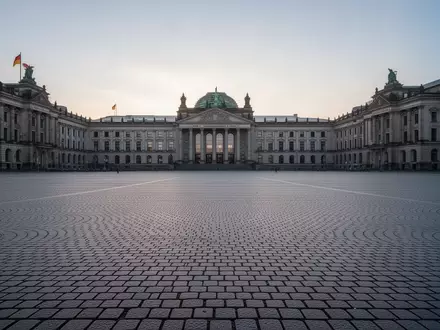 Ein weitläufiger, leerer Stadtplatz mit historischem Kopfsteinpflaster und neoklassizistischer Architektur im morgendlichen Licht. - Foto: über boerse-global.de