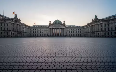 Ein weitläufiger, leerer Stadtplatz mit historischem Kopfsteinpflaster und neoklassizistischer Architektur im morgendlichen Licht. - Foto: über boerse-global.de