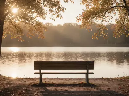 Eine leere Parkbank vor einem ruhigen See im goldenen Abendlicht. - Foto: ĂĽber boerse-global.de